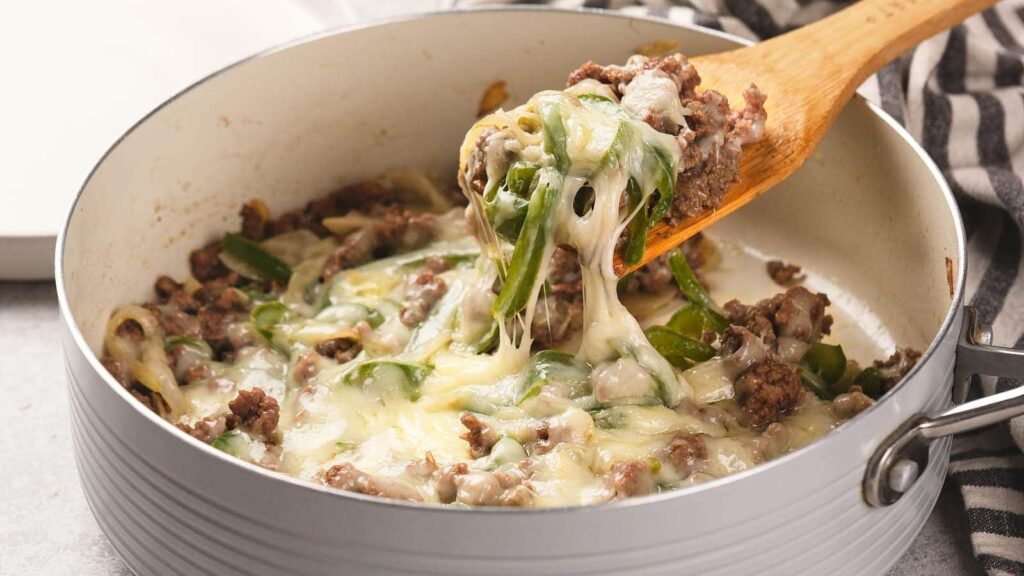 A wooden spoon lifting a portion of cheesy ground beef philly cheeseteak.