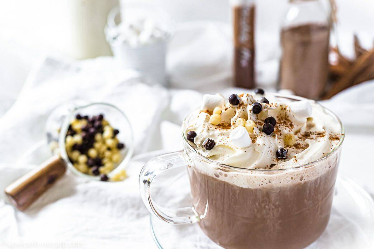 A glass mug of hot chocolate topped with whipped cream, mini marshmallows, and chocolate chips.