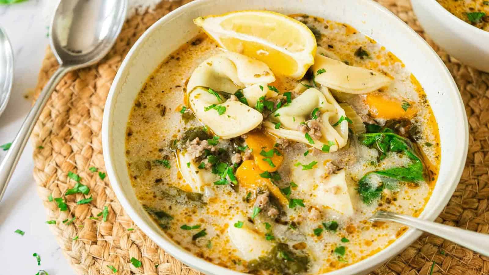 Creamy soup with vegetables and herbs in a white bowl, next to a spoon and a striped towel.