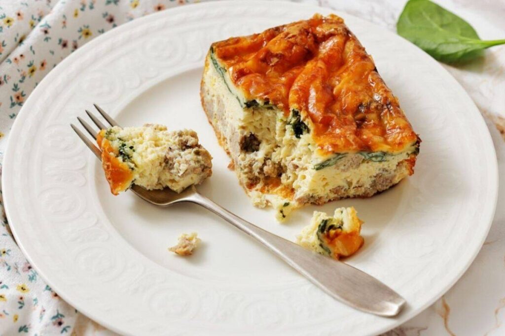 A slice of Egg Breakfast Casserole on a white plate with a fork.