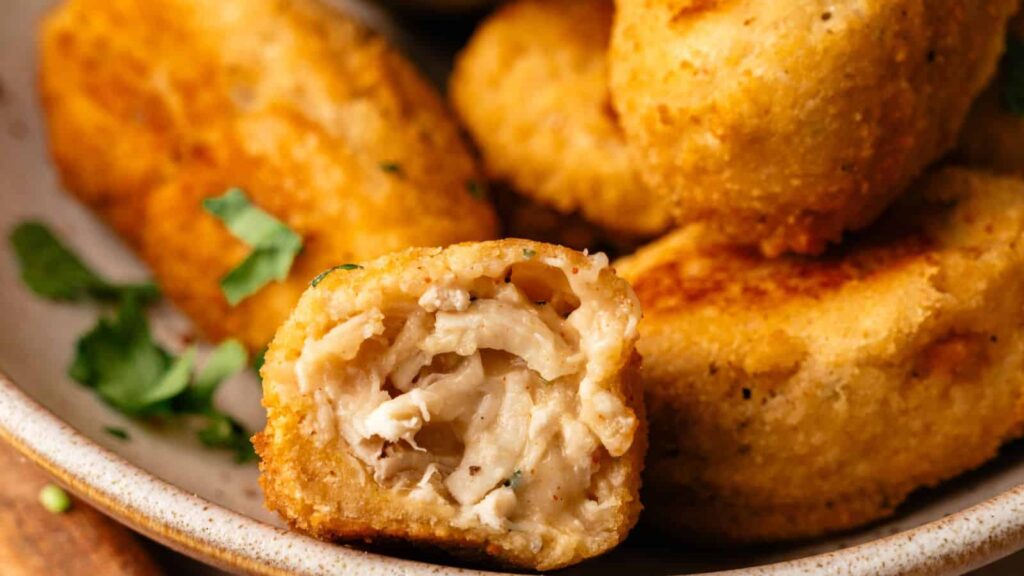 Close-up of several breaded chicken nuggets on a plate, with one nugget bitten in half to show the cooked chicken filling inside.