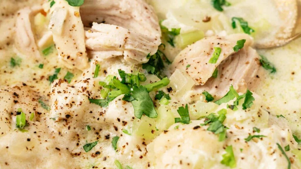Close-up of a creamy chicken and dumpling soup, garnished with chopped parsley and ground black pepper.