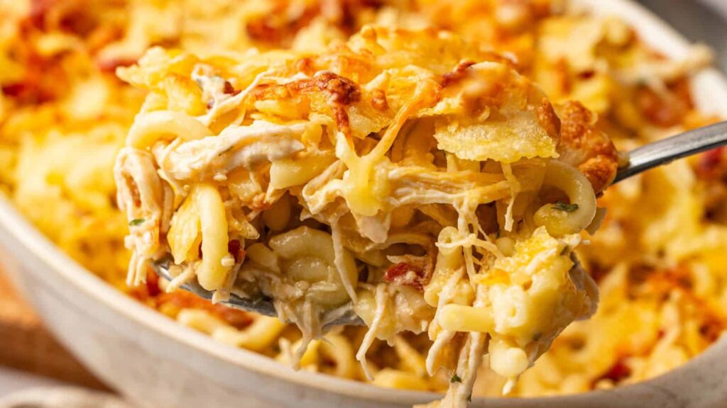 A close-up of a spoonful of baked cheesy pasta casserole with shredded chicken and golden melted cheese on top.