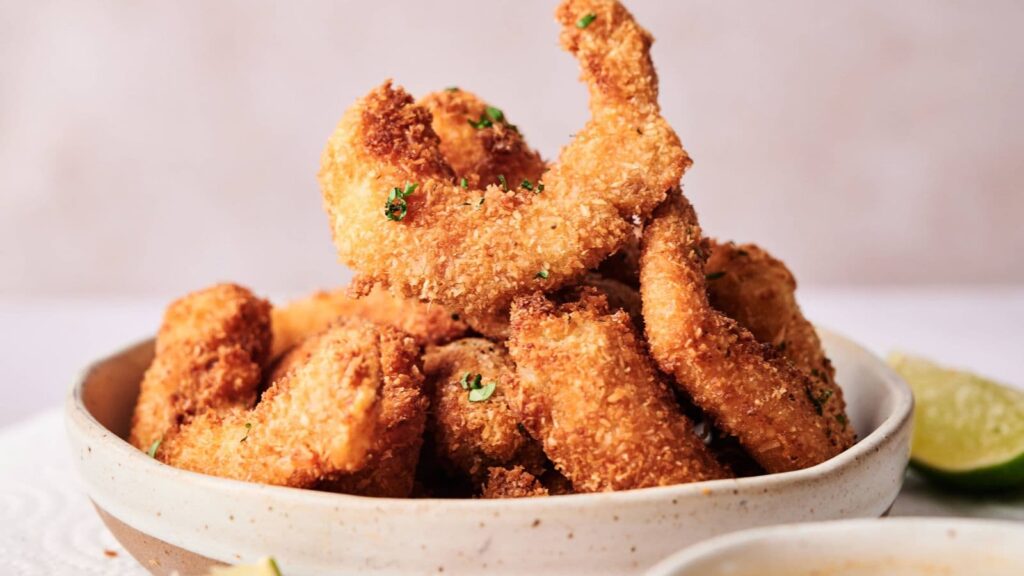 A bowl filled with golden-brown, breaded and fried shrimp, garnished with chopped herbs.