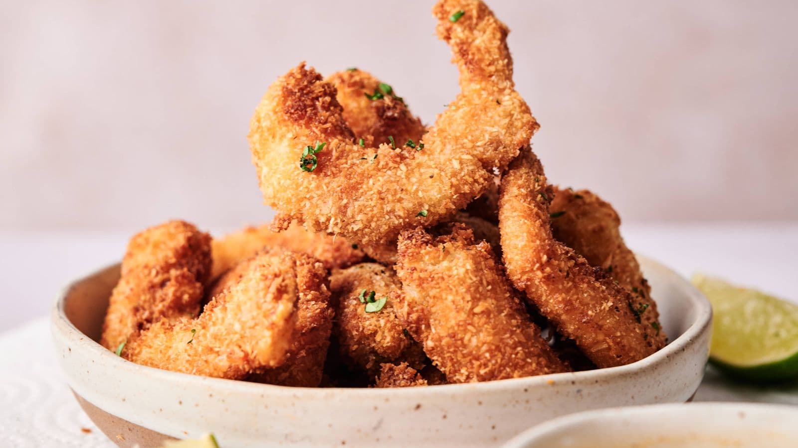 A bowl filled with golden-brown, breaded and fried shrimp, garnished with chopped herbs.