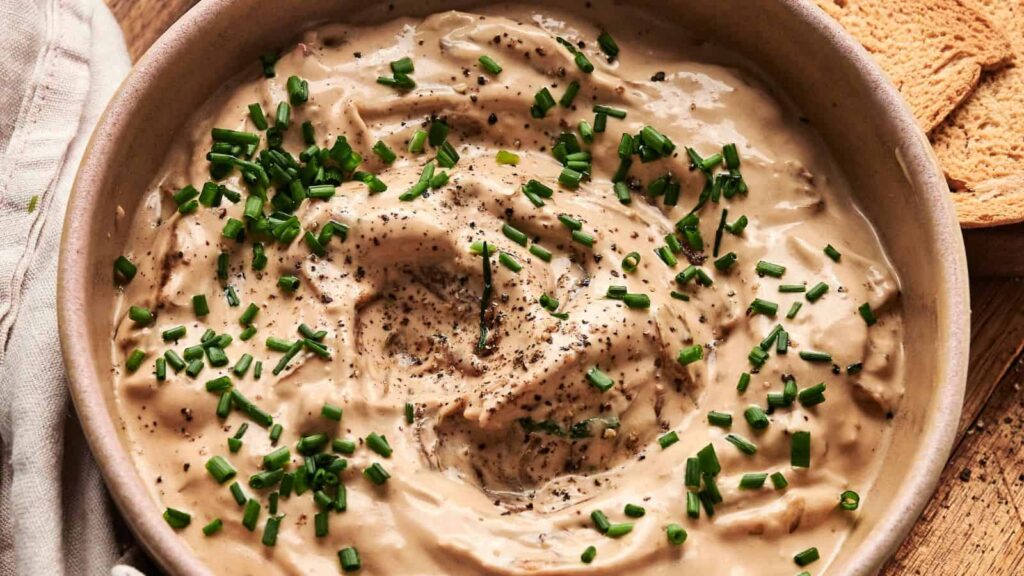 A bowl of creamy dip topped with chopped chives and cracked black pepper.
