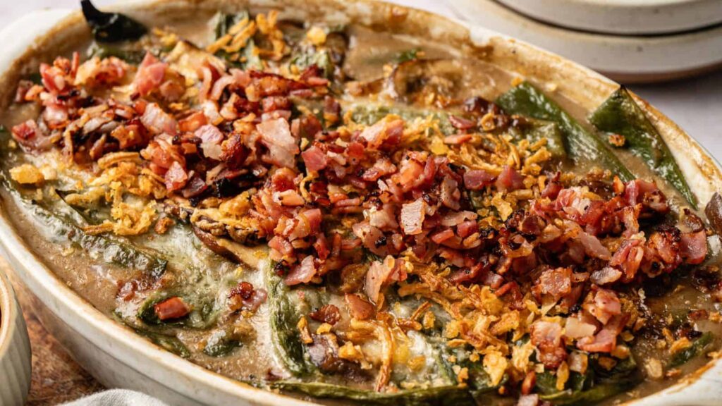 A baked casserole topped with chopped bacon, crispy onions, and melted cheese, featuring visible green peppers and a creamy sauce.