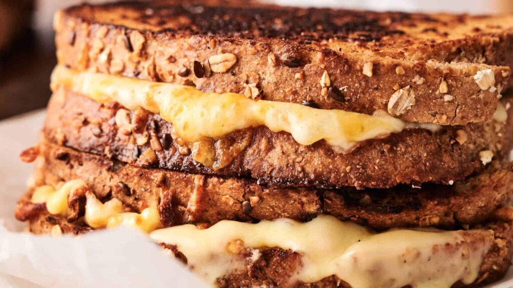 Close-up of two grilled cheese sandwiches made with multigrain bread and melted cheese, stacked on top of each other.