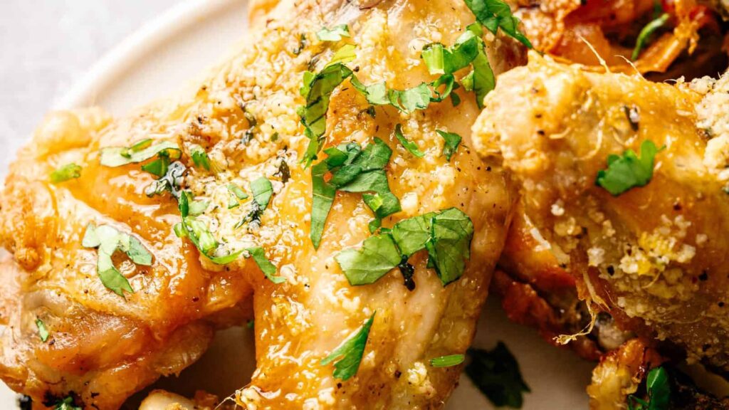 Close-up of seasoned baked chicken wings garnished with chopped fresh parsley on a white plate.