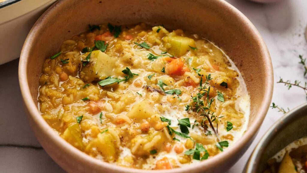 A bowl of thick lentil and vegetable soup garnished with fresh herbs, featuring visible chunks of carrots and potatoes.