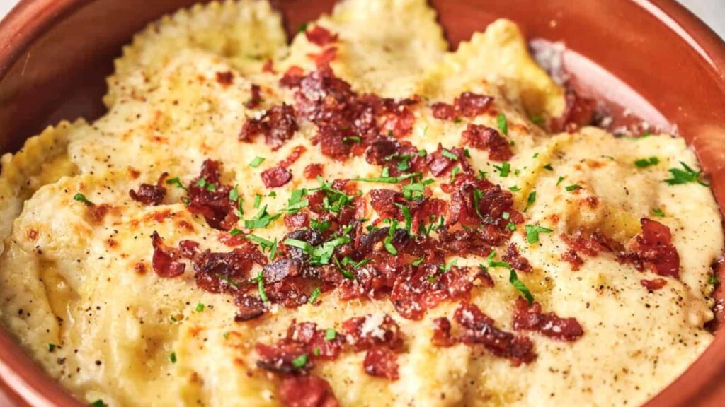 A dish of ravioli topped with grated cheese, bacon bits, and chopped parsley.