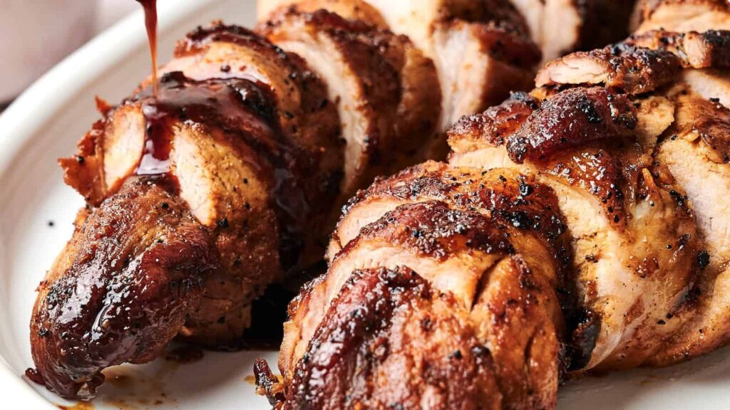 Close-up of grilled, sliced pork tenderloins drizzled with a dark brown sauce on a white plate.
