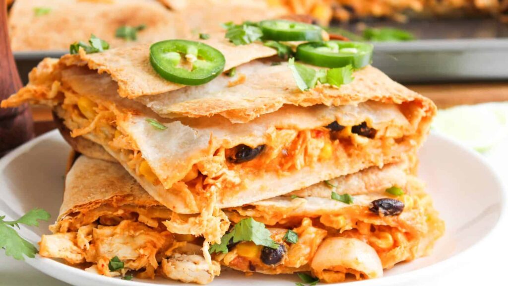 Close-up of sliced quesadillas filled with chicken, cheese, and black beans, topped with jalapeño slices and cilantro on a white plate.