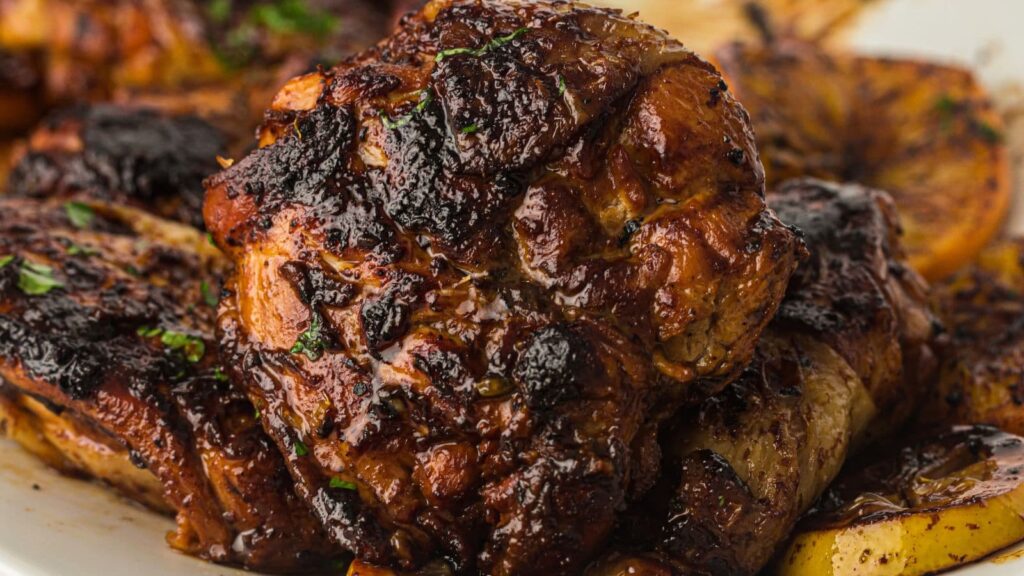 Close-up of a piece of grilled, charred meat garnished with herbs and served with roasted potatoes on a white plate.