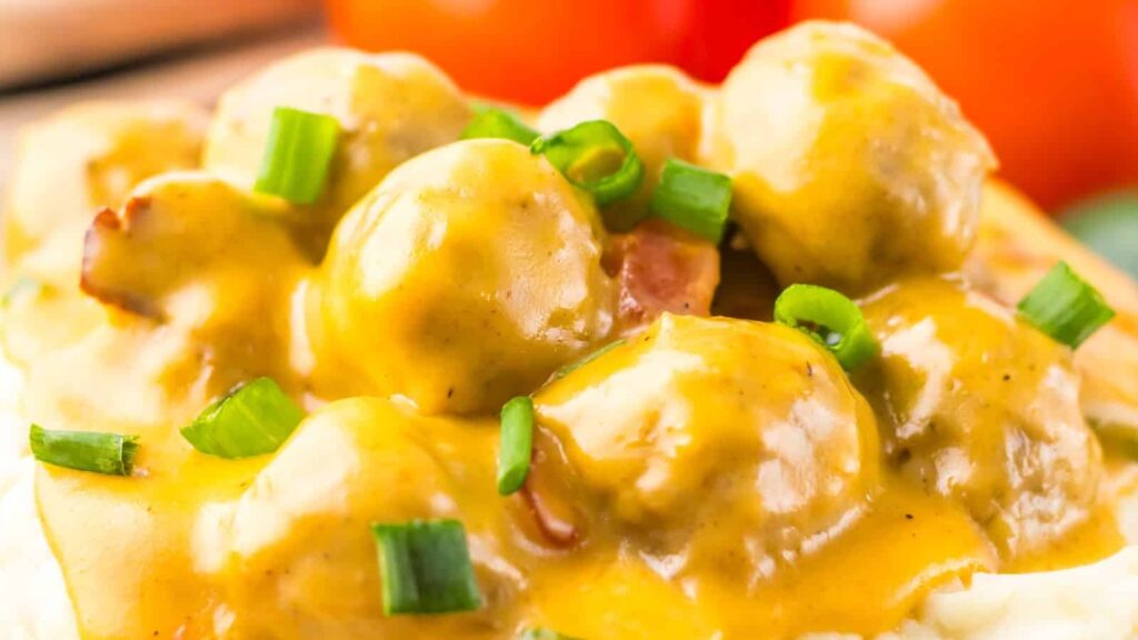 Close-up of meatballs covered in a creamy yellow sauce, garnished with chopped green onions.