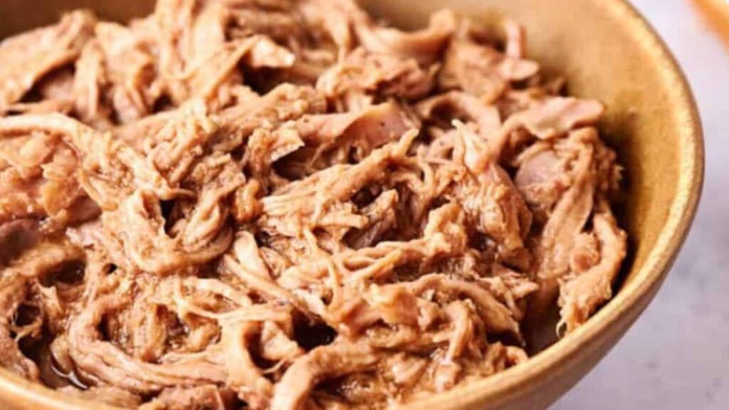 Close-up of shredded, cooked pork in a brown bowl.