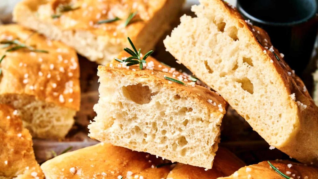 Close-up of sliced focaccia bread topped with coarse salt and rosemary, showing its airy texture.