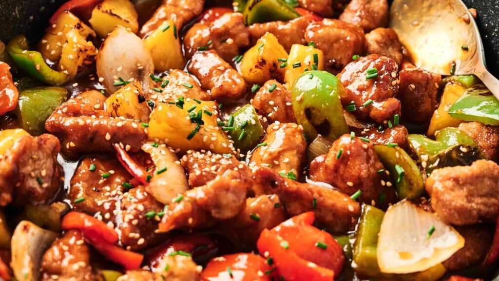 Stir-fried dish with sesame seeds, bell peppers, onions, and bite-sized meat pieces in a glossy sauce.