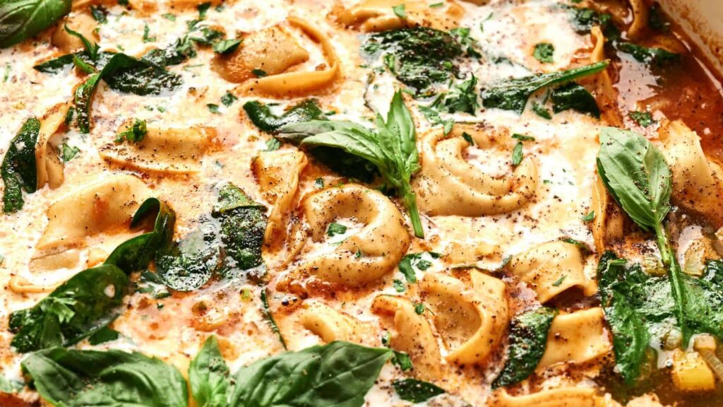 Close-up of tortellini in a creamy tomato sauce with spinach and fresh basil leaves.