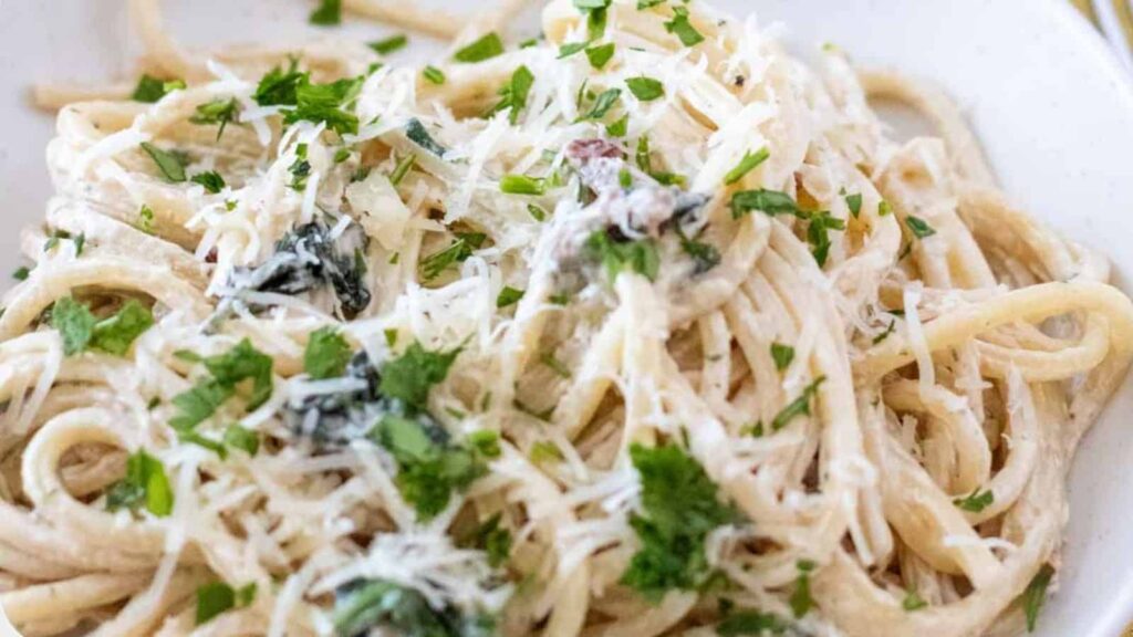 A close-up of a plate of creamy pasta topped with grated cheese and chopped parsley.