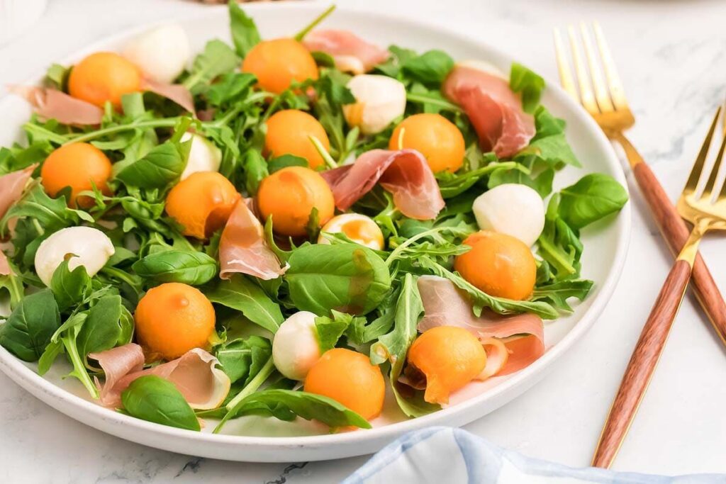 Melon prosciutto salad with arugula, cantaloupe, mozzarella, and prosciutto, ready to serve.