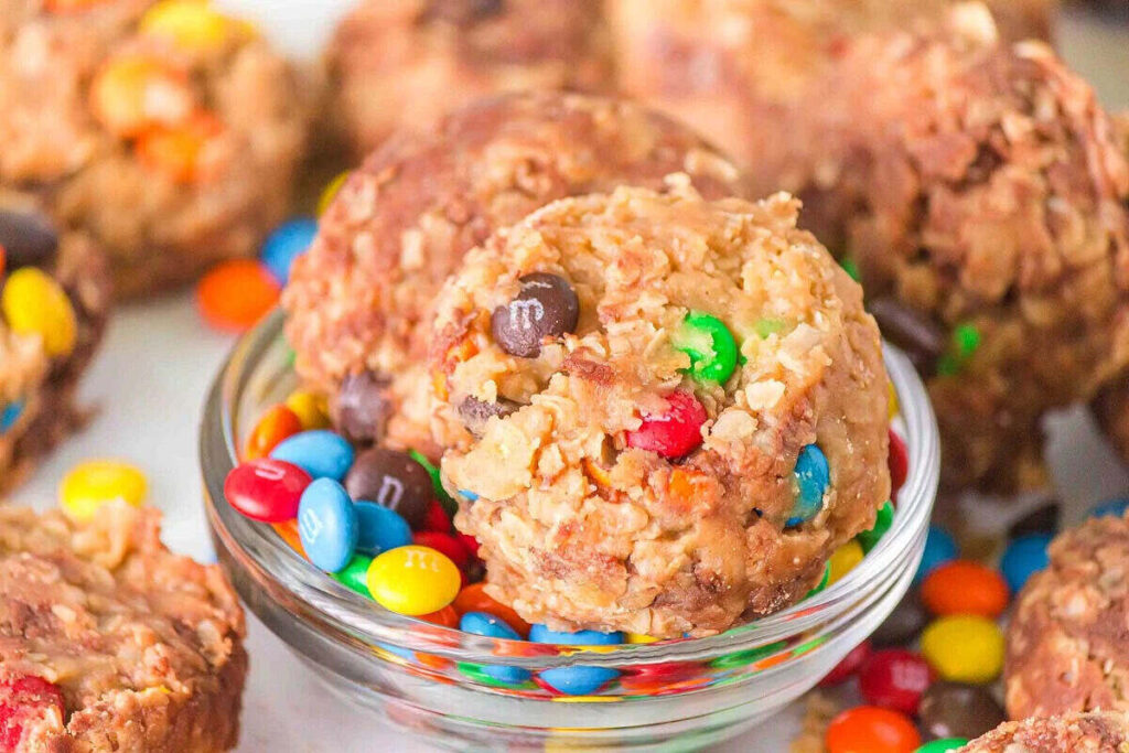 A bowl of colorful candy-coated chocolates surrounded by no-bake monster cookies.