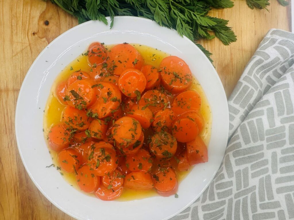 A plate of glazed carrot slices topped with chopped herbs, served with a light sauce.