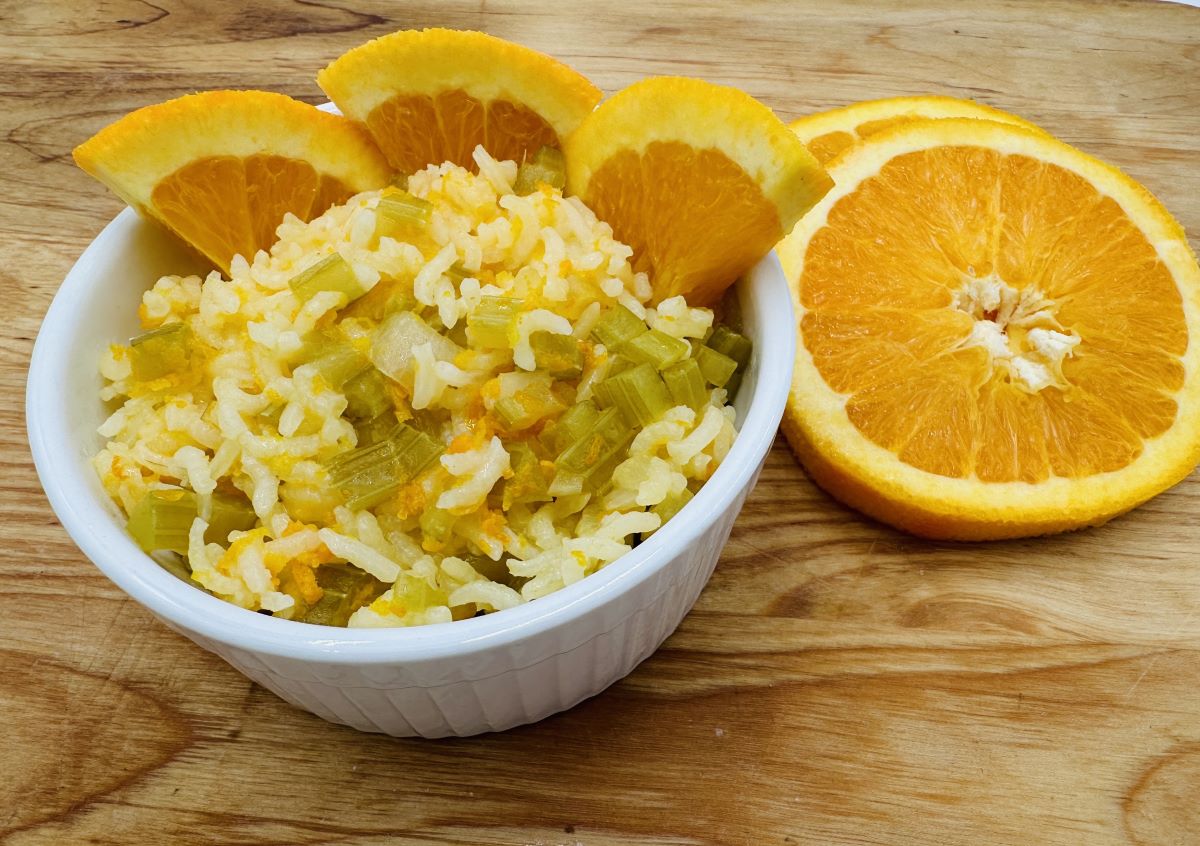 White rice with chopped celery in white bowl with orange slices along the back.