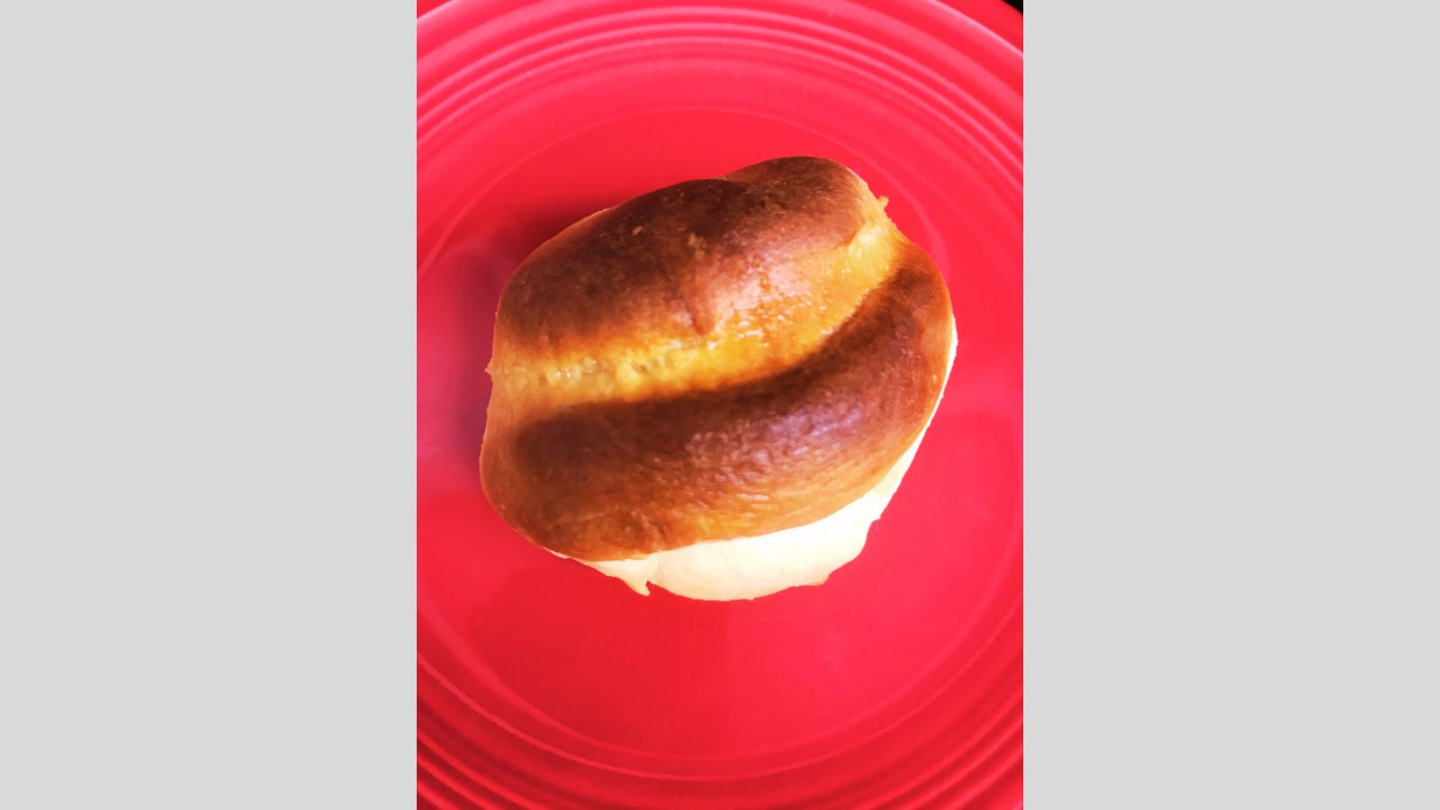 A golden-brown Parker House roll with a split top sits on a red plate, viewed from above.
