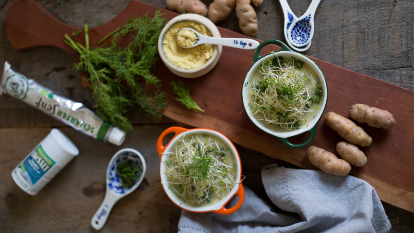 Two bowls of soup with dill on a wooden cutting board.