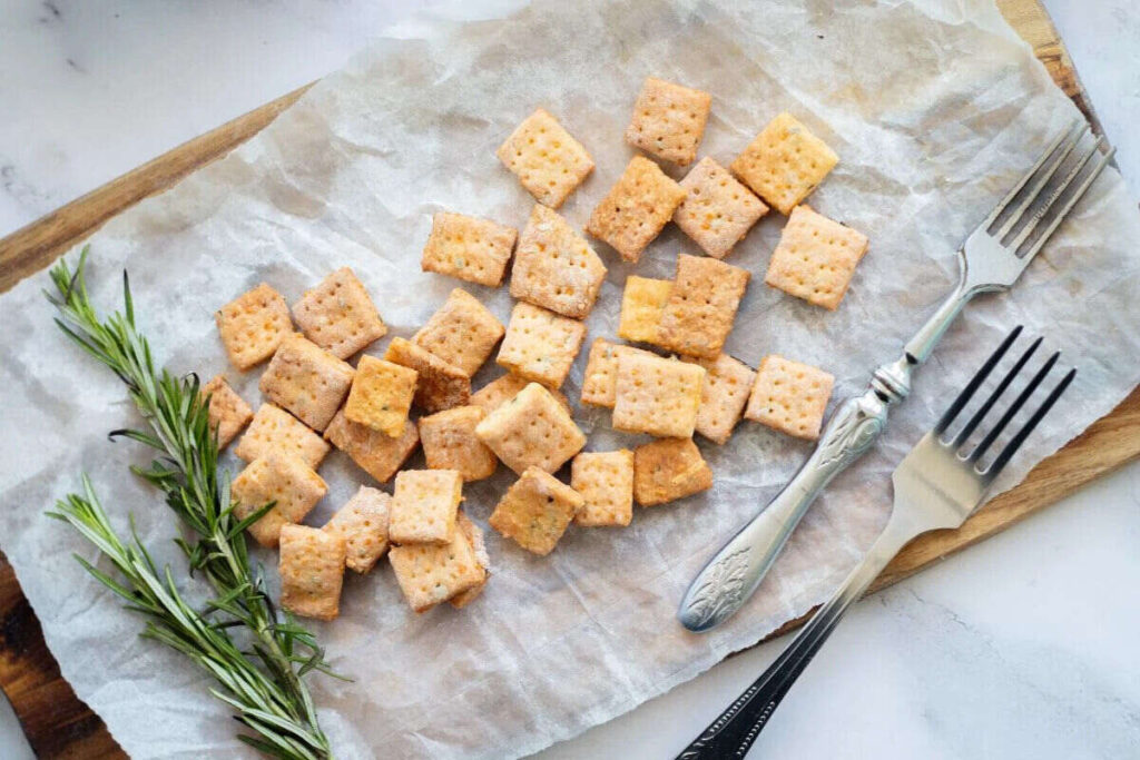 Rosemary cheddar crackers on a wooden board with fresh rosemary and forks.