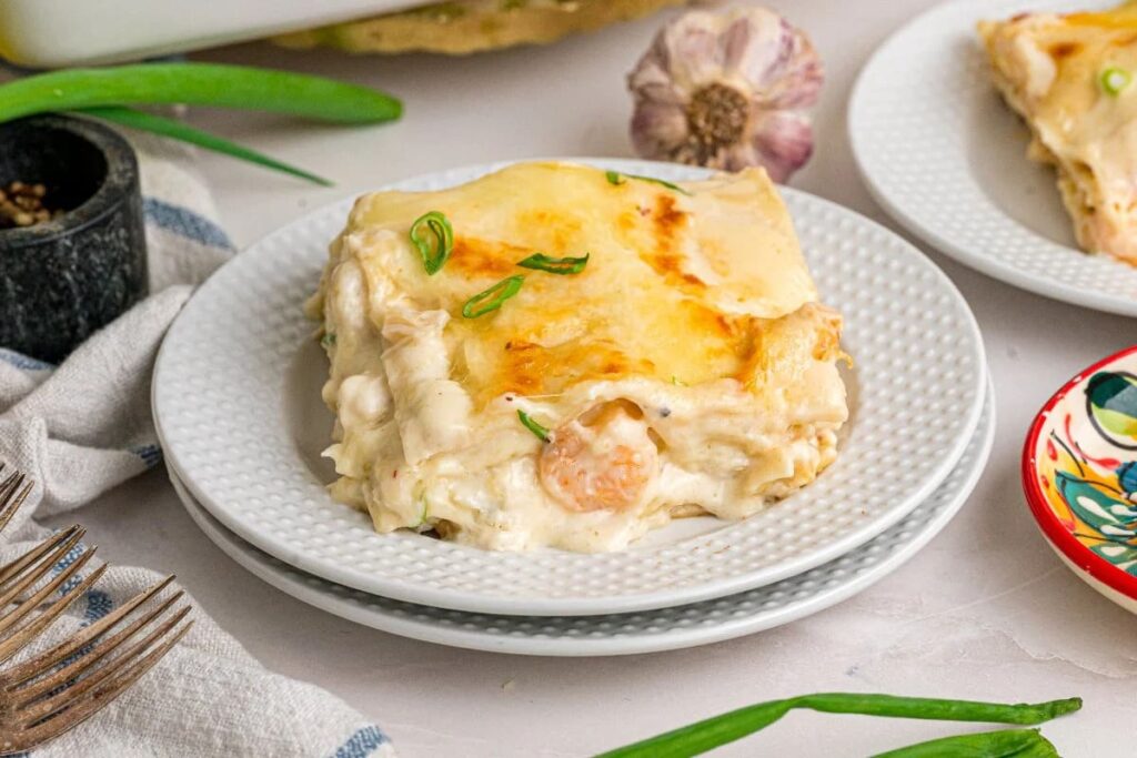 A slice of seafood lasagna with herbs, served on a white plate.