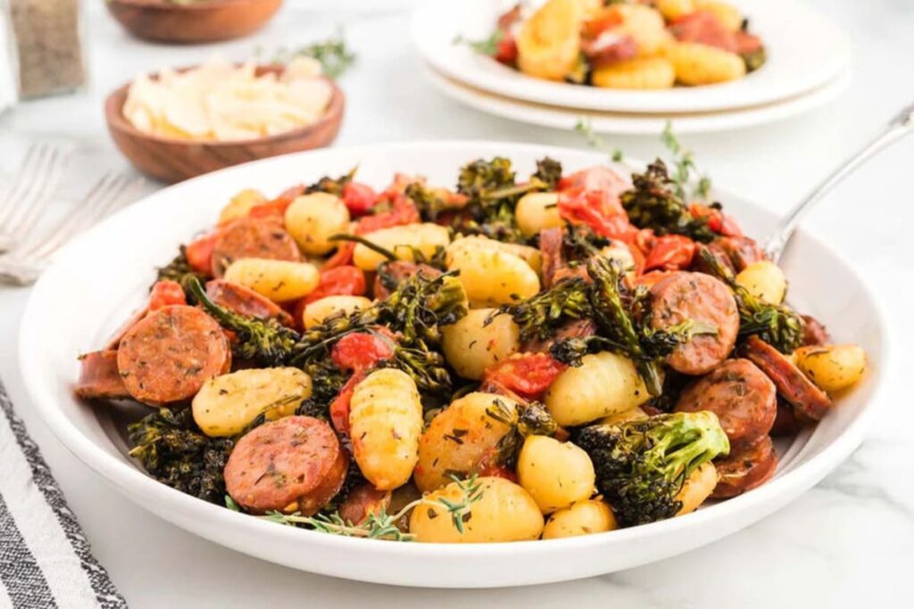 Sheet pan gnocchi and sausage with broccolini and tomatoes, garnished with fresh herbs.
