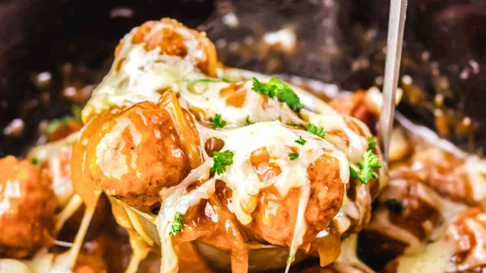 Meatballs topped with melted cheese and chopped parsley in a slow cooker.