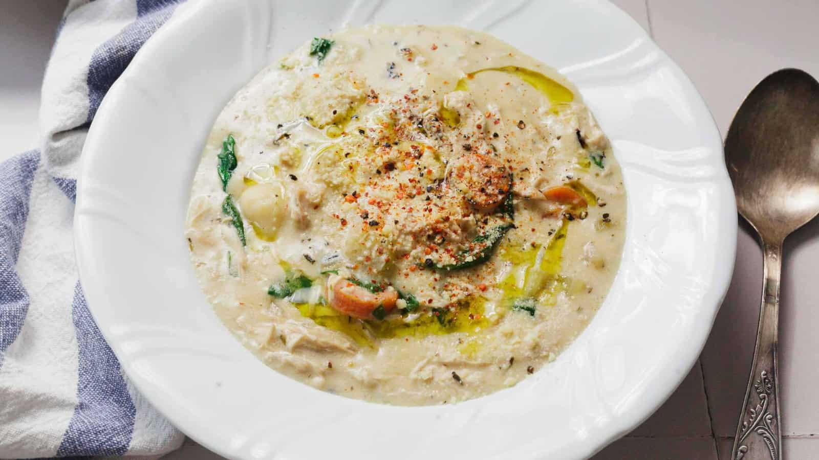 Creamy chicken gnocchi soup with vegetables served in a white bowl, bread and herbs on the side.