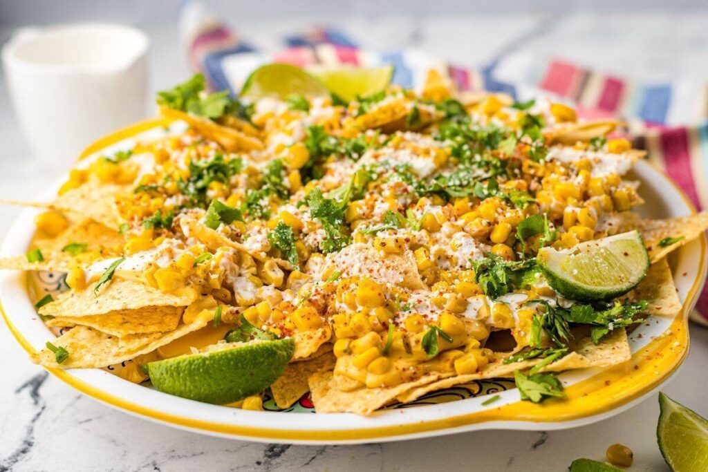Enjoy Street Corn Nachos topped with corn, cheese, crema, cilantro, chili, and lime wedges.