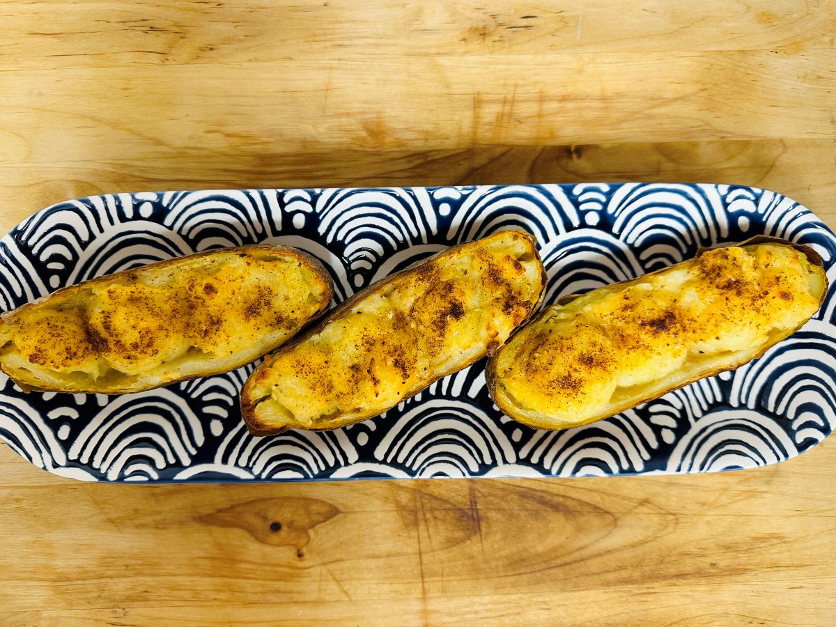 Three stuffed baked potatoes with a golden, seasoned top are arranged on a rectangular plate with a bold black and white geometric pattern, set on a wooden surface.