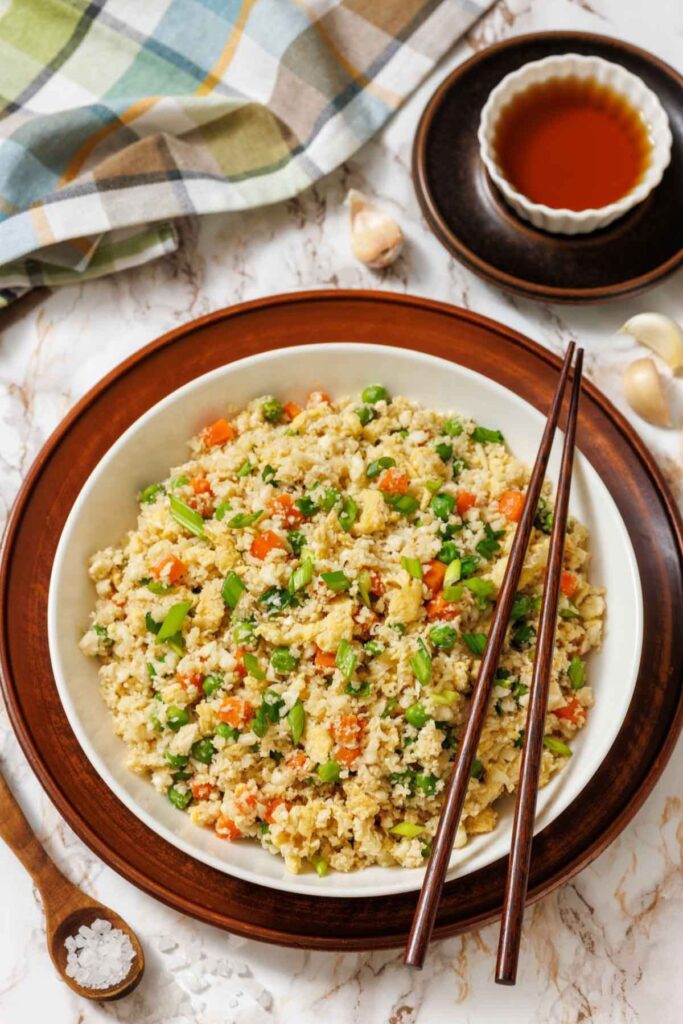 Cauliflower fried rice in a bowl with chopsticks and soy sauce on the side.