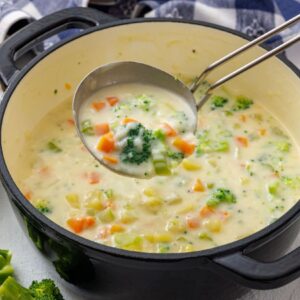 Ladling vegetable chowder with broccoli and carrots from a pot.