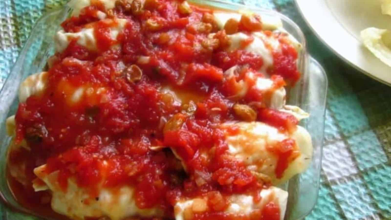 A glass baking dish filled with cabbage rolls topped with tomato sauce and raisins, set on a textured cloth.