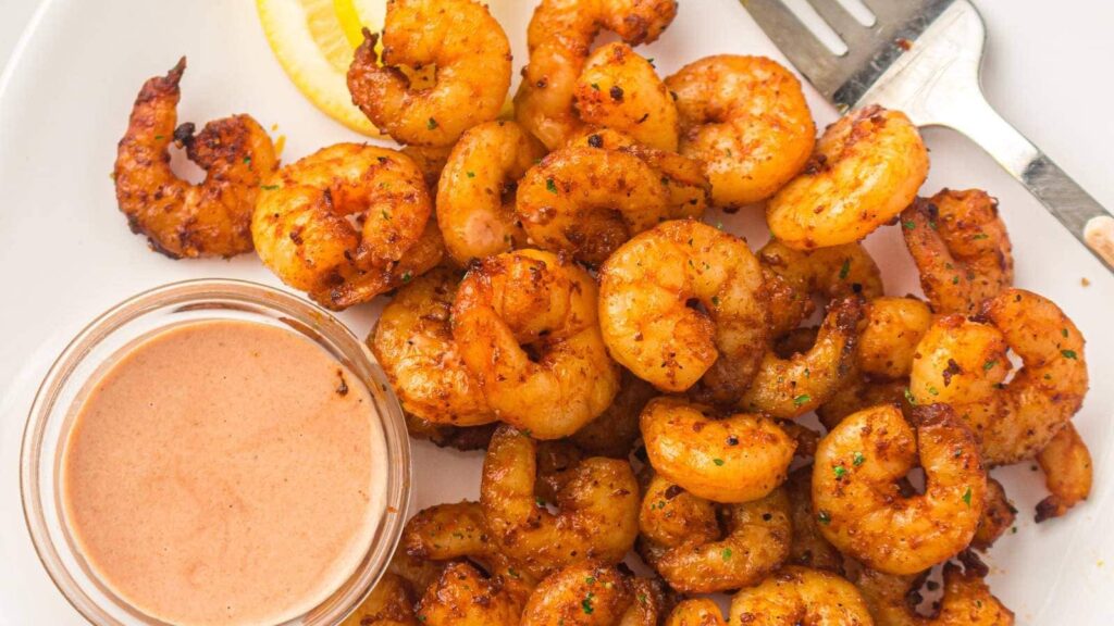 Cooked shrimp on a white plate with a sauce container next to it.