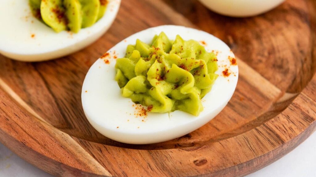 Close-up of a deviled egg half with bright green avocado filling.