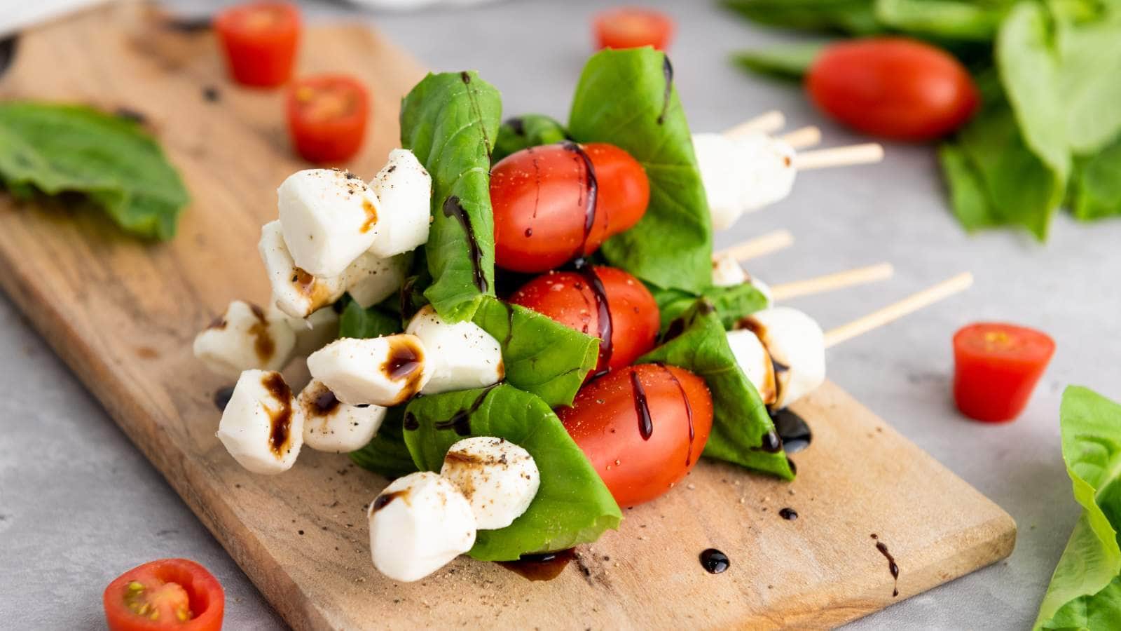 Basil tomato mozzarella skewers on a wooden board, drizzled with balsamic glaze.
