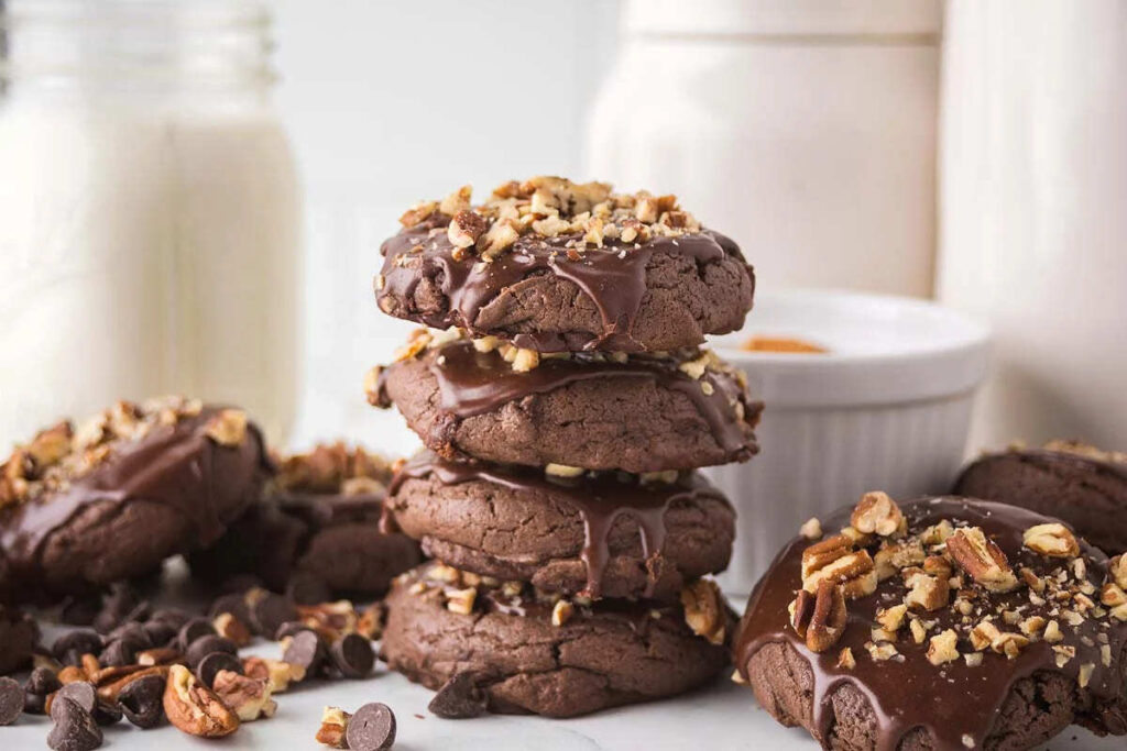 chocolate Texas sheet cake cookies with nuts and chips are stacked next to a jar of milk.