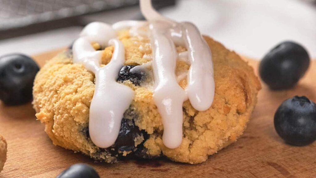 A piece of blueberry scone being drizzled with white frosting.