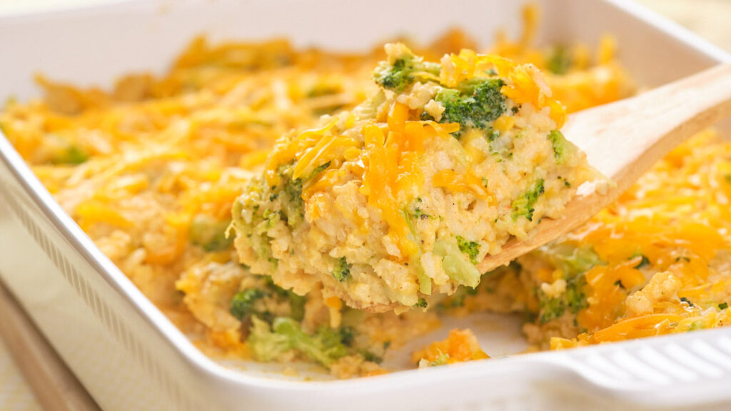 A wooden sppon lifting up a portion of broccoli rice casserole.