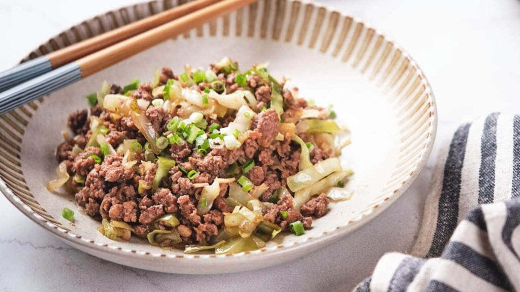 A bowl of cabbage stiry fry, with a pair of chopsticks resting on top.