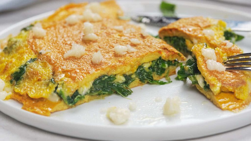 Golden spinach and feta omelet served on a white plate with a section cut away showing the filling.