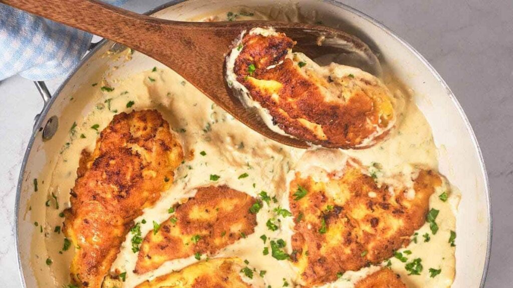 A wooden spoon resting in a pan of chicken francese