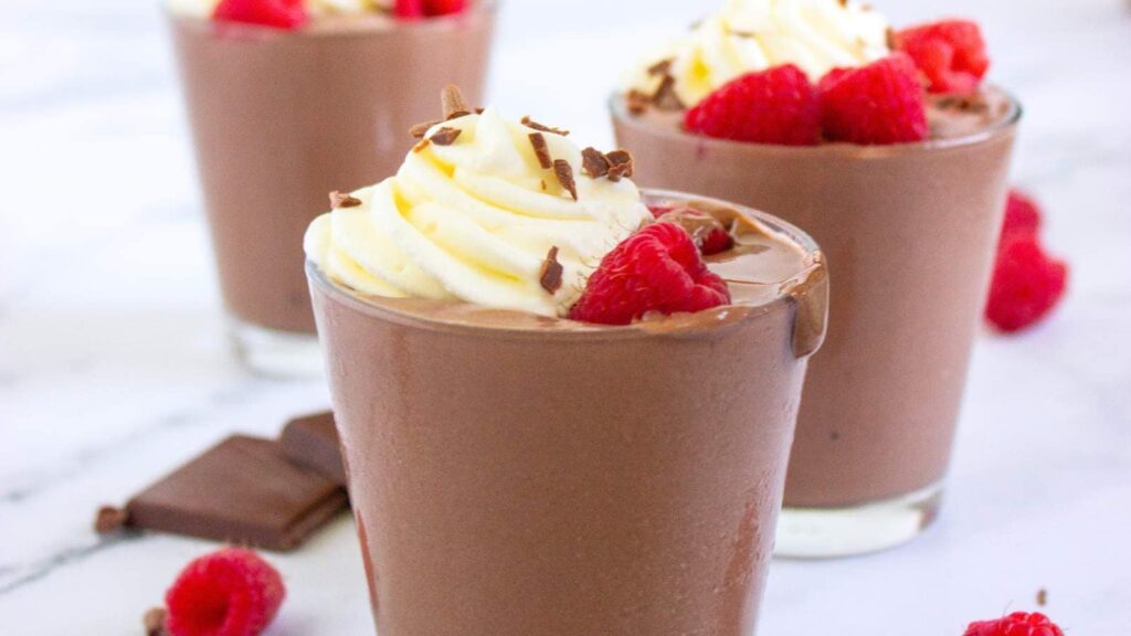 Two glasses of chocolate pudding topped with raspberries and whipped cream.